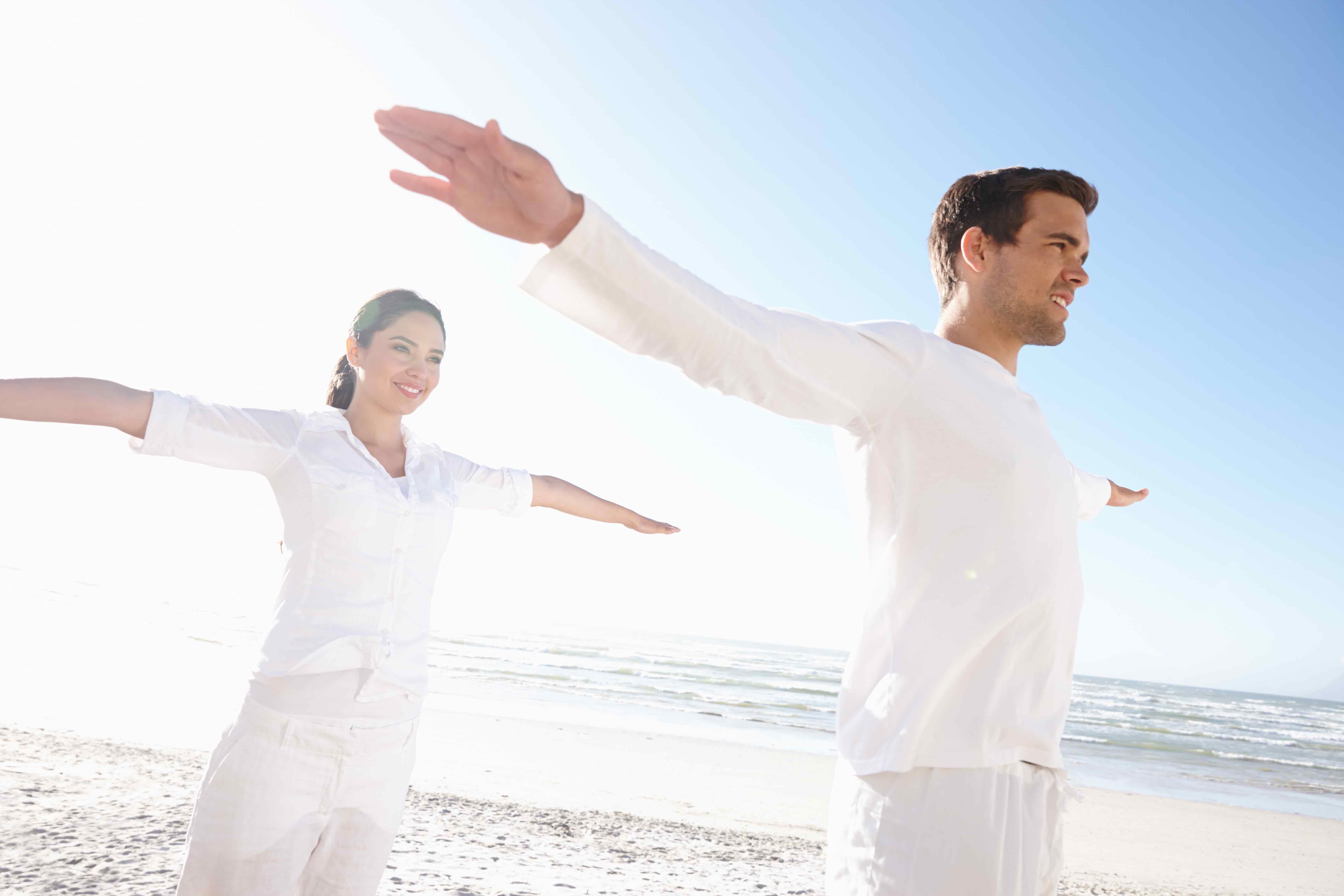 A couple stretching on the beach under sunny skies