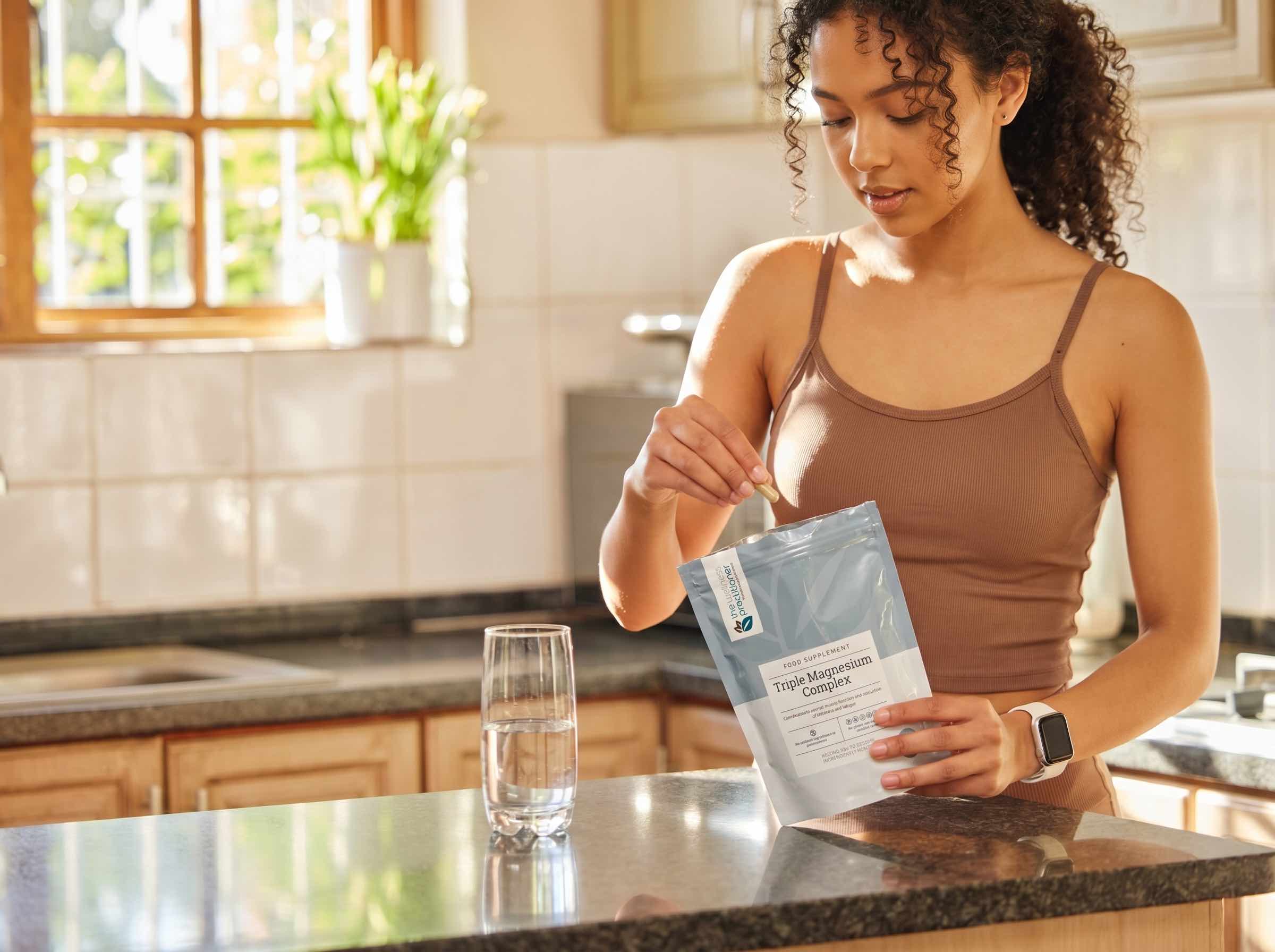 A woman taking a Triple Magnesium Complex capsule in her kitchen